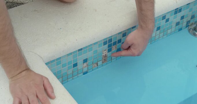 swimming pool wall with broken and missing mosaic tiles. Highlights structural damage, poor maintenance, and safety concerns in a resort or hotel environment.