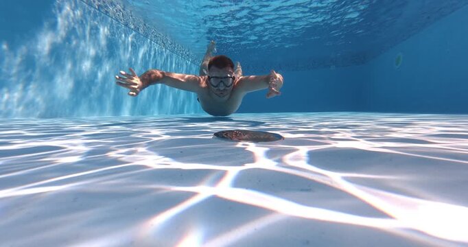 A man diving underwater in a swimming pool to inspect or check the pool filter system. Focus on maintenance, technical inspection, and underwater pool service work.O