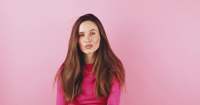 Attractive young woman posing with confidence and flirty smile, touching long brunette hair, expressing joy and feminine beauty, studio portrait isolated on vibrant pink background, morning routine