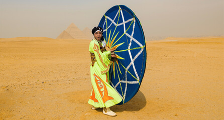Fototapeta premium Theatrical folk dancer in colorful green costume performing a dynamic spinning skirt dance pose in the desert near the Giza pyramids ideal for
