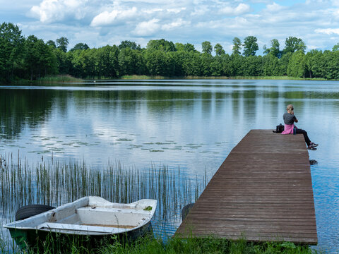A woman sitting on a wooden bridge over a lake in late spring. Spring is the season.