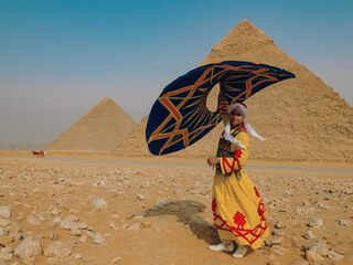 Fototapeta premium Joyful Egyptian tanoura folk dancer twirling a colorful skirt overhead before the Giza pyramids in the sunlit desert ideal for Egypt tourism culture