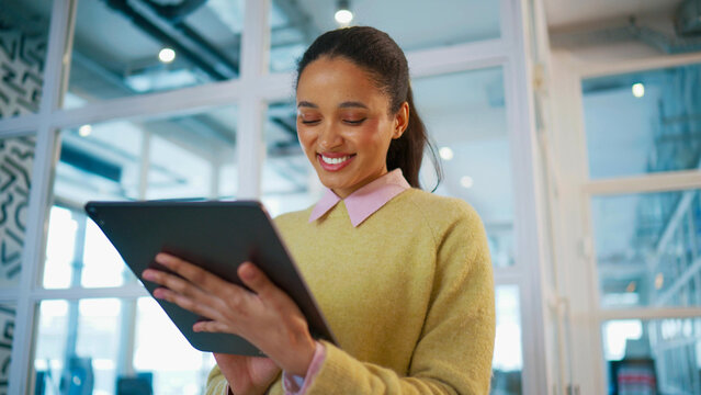Successful business woman holding tablet and smiling while reading message. Standing near glass office wall. Female checking online project updates. Corporate technology lifestyle concept.