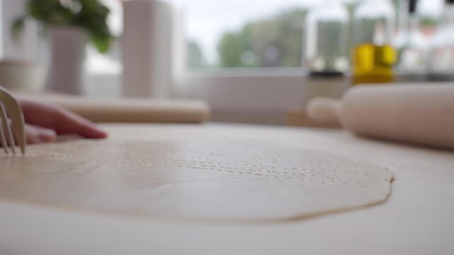 Hand pricks rolled dough with fork on kitchen counter. Concept of home baking and pastry preparation