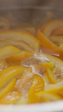 Orange peel pieces cook in syrup inside a saucepan. Concept of candied orange peel and homemade sweets