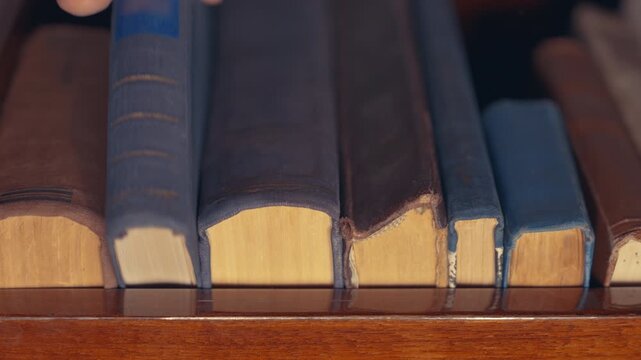 Hand Taking Antique Book from Library Shelf &mdash; Slow Motion Close-Up | Worn Hardcover Spines on Wooden Shelf Viewed from Below | Vintage Knowledge Concept