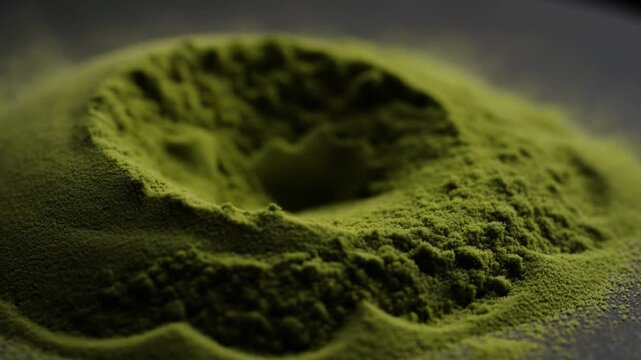 Close-up of shallow crater forming in fine olive green powder with raised rim and steep inner walls, low-angle soft directional lighting emphasizing granular texture and depth