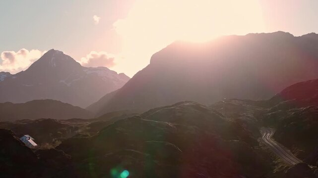 Sunlit mountain pass with winding road and distant snow peaks