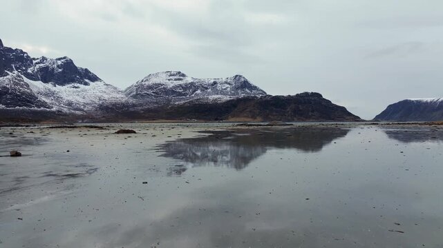Reflective tidal shoreline with rocky headland and snow-dusted mountains