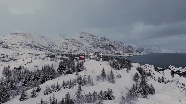 Red cabin on snowy coastal ridge near mountains and sea