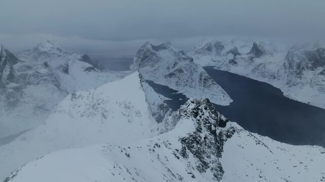Aerial view of snowy mountain ridge leading to jagged peaks and fjord