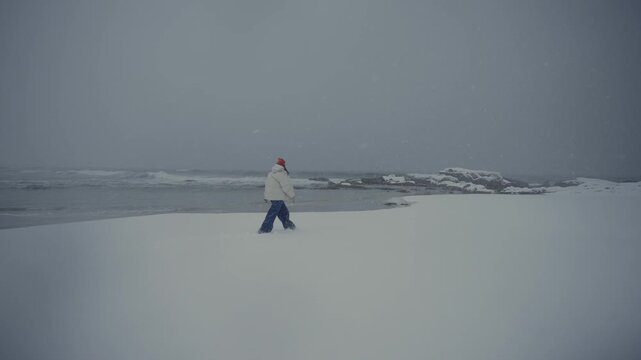 Solitary person walking on snowy coastal beach under overcast sky
