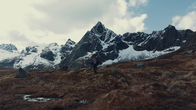 Solitary hiker walking across tundra toward jagged snow mountains