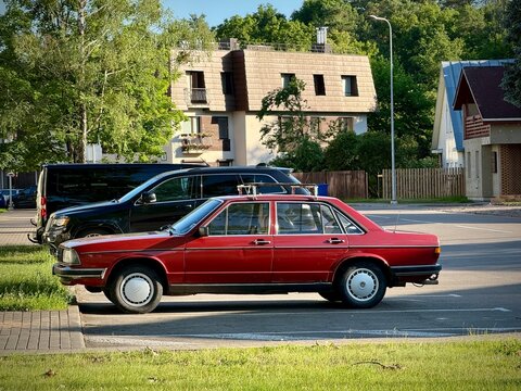 Red Audi 100 C2 parked on a street with trees and residential buildings in the background. The car features a classic 1970s design with a boxy shape and chrome accents. 