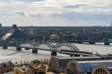 Daily city crossings as a passenger train moves across the steel railway bridge over Daugava River in Riga for commuting and urban connectivity themes. Copy space © Nimbus Works