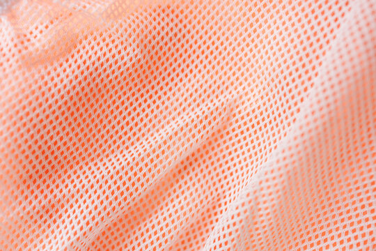 White mesh fabric over bright orange textile creating breathable sports material texture