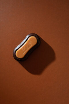 LINDT filled chocolate praline with caramel top on brown background seen from above