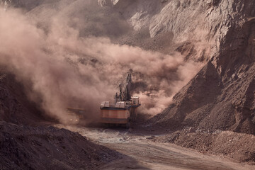 An electric rope shovel stands at the heart of an open pit mine, enveloped in a billowing cloud of dust and displaced earth, a dramatic testament to the scale of modern mining operations in one of the © Beto Santillan
