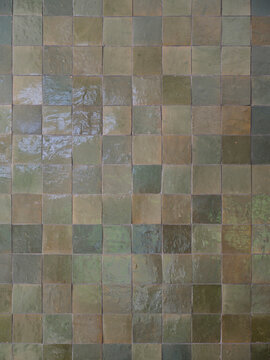 Background of glazed green and earth toned square ceramic tiles, a handmade zellige style wall surface with subtle color variation