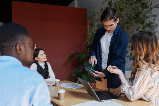 Business professionals collaborating and presenting data to colleagues on a digital tablet at an informal office meeting, fostering communication and teamwork