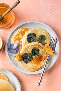 Top view of homemade pancakes with embedded edible pansy flowers and honey butter