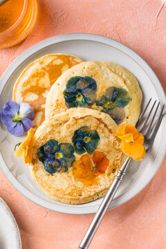 Top view of homemade pancakes with embedded edible pansy flowers and honey butter