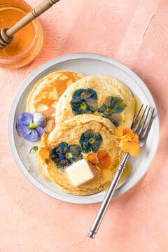 Top view of homemade pancakes with embedded edible pansy flowers and honey butter