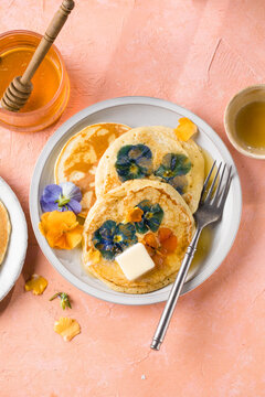 Top view of homemade pancakes with embedded edible pansy flowers and honey butter