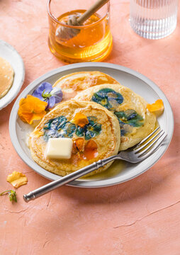 Top view of homemade pancakes with embedded edible pansy flowers and honey butter