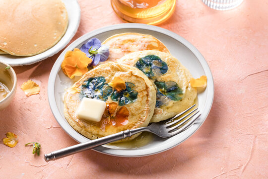 Top view of homemade pancakes with embedded edible pansy flowers and honey butter