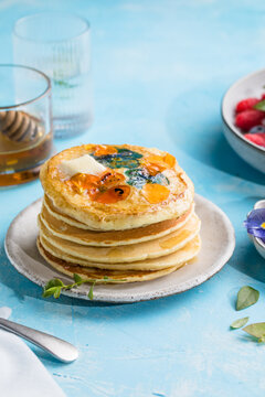Top view of homemade pancakes with embedded edible pansy flowers and honey butter