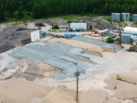 Aerial view of an asphalt mixing plant with large piles of gravel and sand, industrial storage tanks, and machinery in Saulkalne, Salaspils Municipality, Latvia.