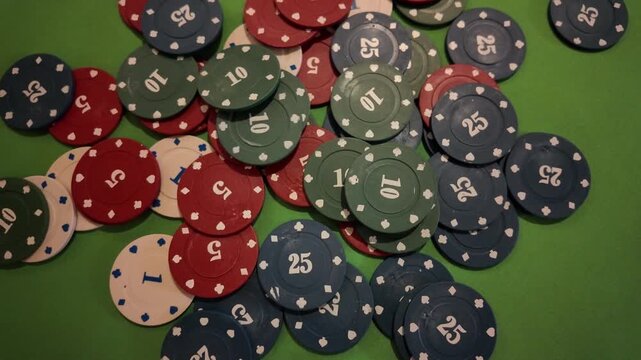 Footage showcases various poker chips, in colors of red, blue, and green, scattered across a vibrant green felt table. Additional chips lightly drop onto the pile, increasing the potential stake. This
