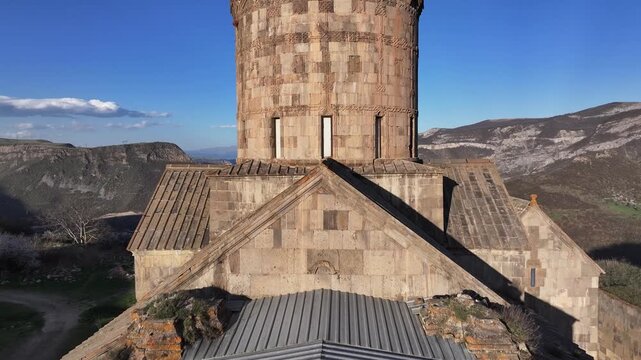 A stunning aerial shot of the ancient Tatev Monastery perched on a cliff edge, surrounded by green mountains and snowy peaks in the scenic Syunik province of Armenia.

