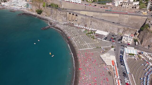 Aerial view of Spiaggia di Meta sandy beach packed with colorful umbrellas along Lungomare Meta di Sorrento with retaining wall, viaduct, and parking, Naples, Italy