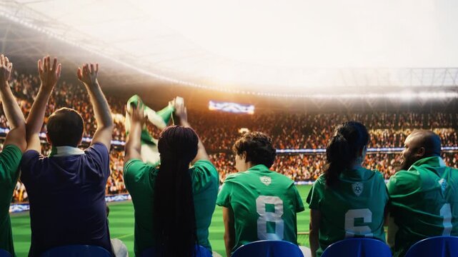 Close up of soccer fans starting crowd wave across sports arena stands during match, showing back view of supporters rising in sequence, doing choreography to create electrifying stadium atmosphere.