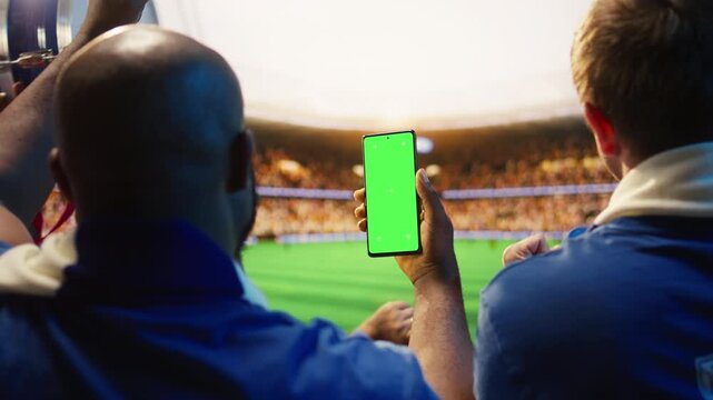 Close up of mockup smartphone used by man in soccer stadium stands to compare match odds, showing football supporter checking live score application predictions on chroma key phone.