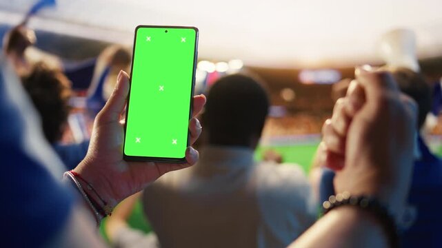 Close up of isolated screen mobile phone used by soccer fan to compare match odds, cheering in stadium, showing football supporter checking live score app predictions on chroma key smartphone.