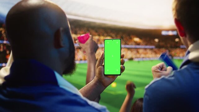 Green screen phone used by man celebrating winning football match bet, pumping fists, showing soccer fan in stadium holding mockup smartphone, feeling pleased by correct prediction.