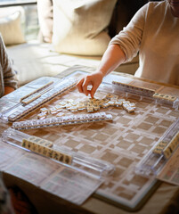 Mahjong game in play on the table with players choosing tiles and keeping score. © Jessica