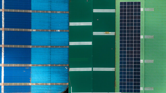 Aerial view of Tecnovia Acores facility rooftops featuring blue and green corrugated metal panels and a large solar panel array in Rabo de Peixe, Acores, Portugal.