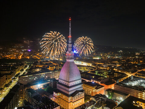 Aerial view of the illuminated Mole Antonelliana landmark surrounded by vibrant fireworks displays over the historic city skyline of Torino, Piemonte, Italy.