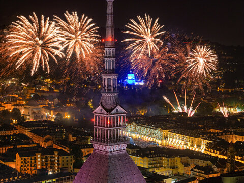 Aerial view of the Mole Antonelliana illuminated at night with vibrant fireworks bursting in the sky above the city of Torino, Piemonte, Italy.
