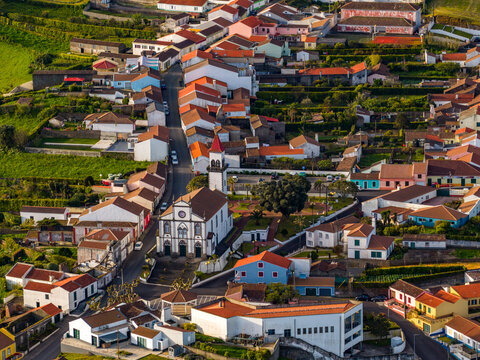 Aerial view of a charming village with a prominent church, colorful houses with red tiled roofs, and lush green fields in the surrounding landscape, Salga, Azores, Portugal.