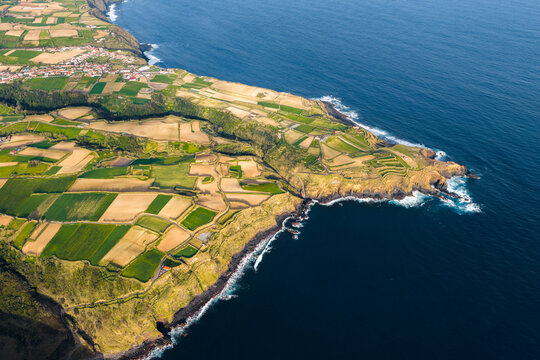 Aerial view of the patchwork agricultural fields and green pastures along the rugged coastline of the Atlantic Ocean in Salga, Azores, Portugal.
