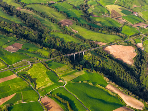Aerial view of a bridge crossing lush green fields and rolling hills in the rural landscape of Salga, Azores, Portugal.