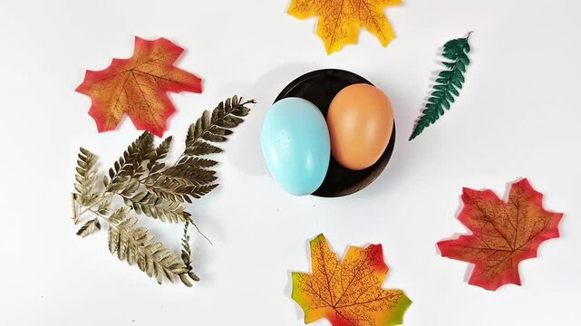 Flat lay of colorful Easter eggs with autumn maple leaves on white background