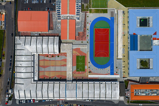 Aerial view of the school complex featuring a sports track, basketball court, and colorful rooftops in Rabo de Peixe, Azores, Portugal.