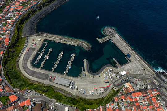 Aerial view of the harbor in Rabo de Peixe with fishing boats docked at the piers, concrete quays, and surrounding coastal town buildings in Rabo de Peixe, Azores, Portugal.