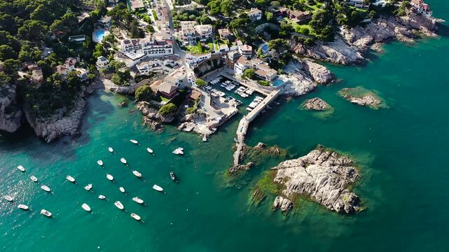 Aerial view of Aiguablava Beach, one of the most beautiful coves on the Costa Brava, featuring crystal-clear turquoise waters, rocky islets and lush Mediterranean pine forests. 
